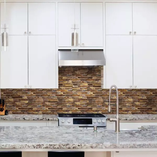 Sparkling interlocking brown glass backsplash with white cabinets, a range hood, and a marble countertop.