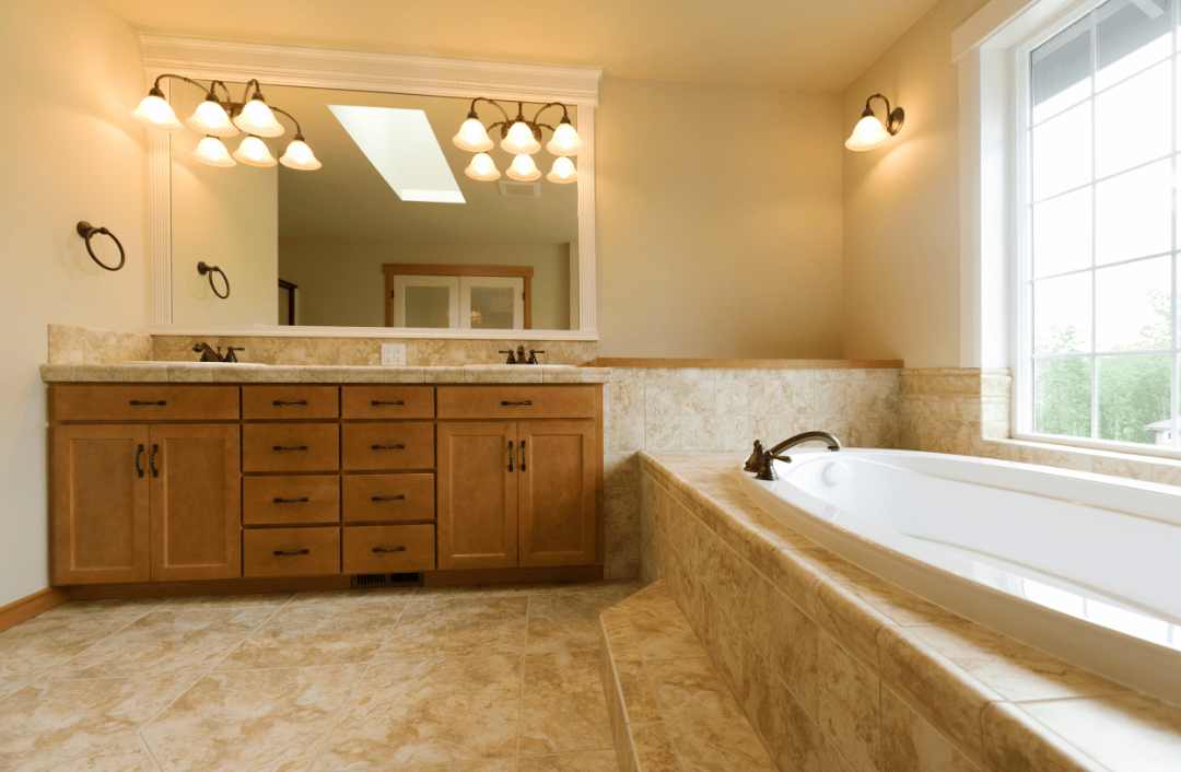An image showing a spacious bathroom with travertine floors and wooden cabinets