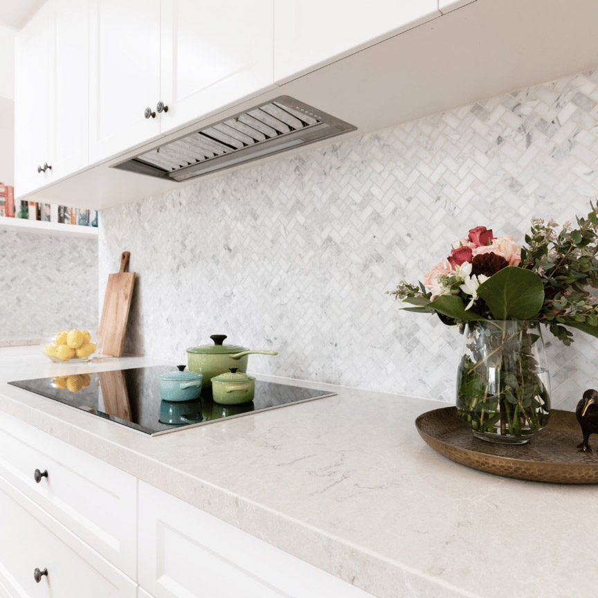 A wall with white and gray tiles in a herringbone pattern and a marble countertop